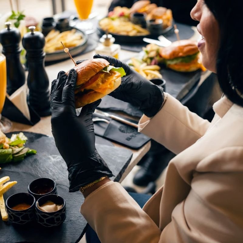 Un burger tenu à deux mains, frites et sauces sur la table