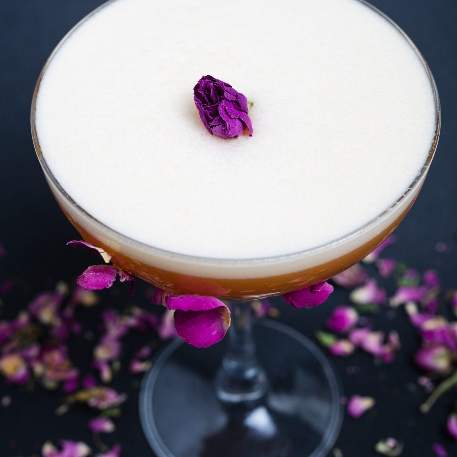 Gros plan sur la mousse blanche d'un cocktail et son pétale de rose