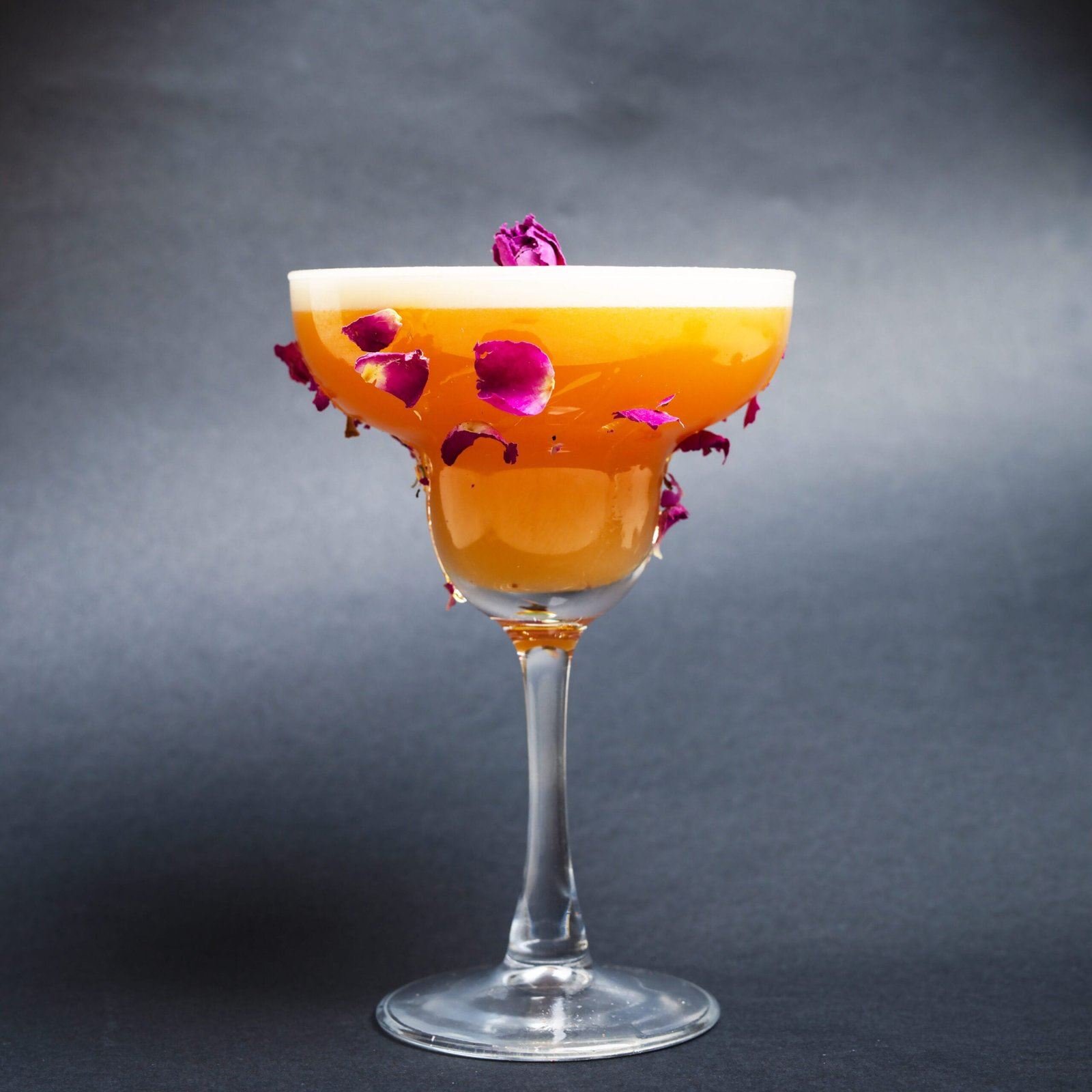 Cocktail orangé couronné de mousse blanche et de pétales de rose séchés