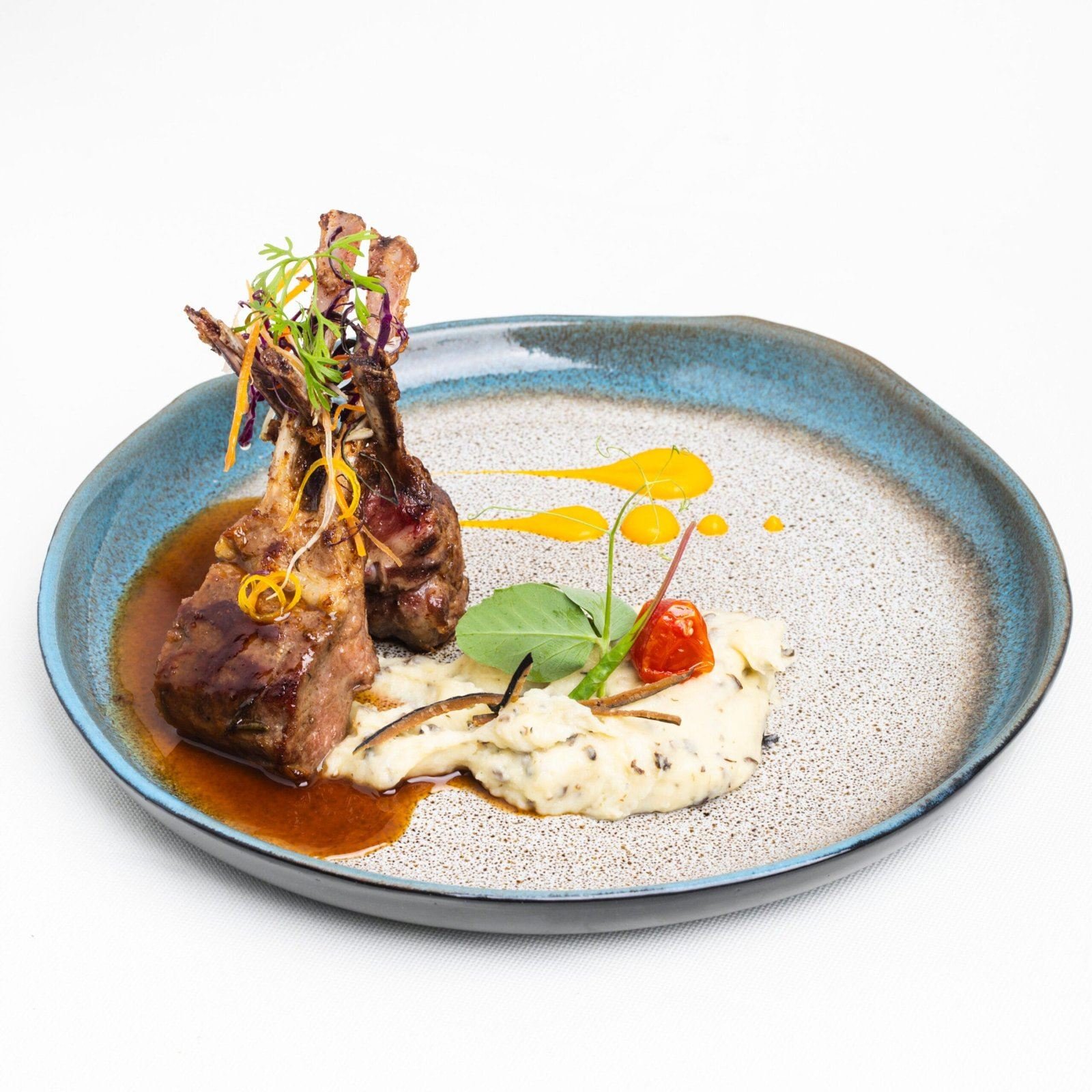 Côtes d'agneau dressées en pyramide sur une purée, jus brun