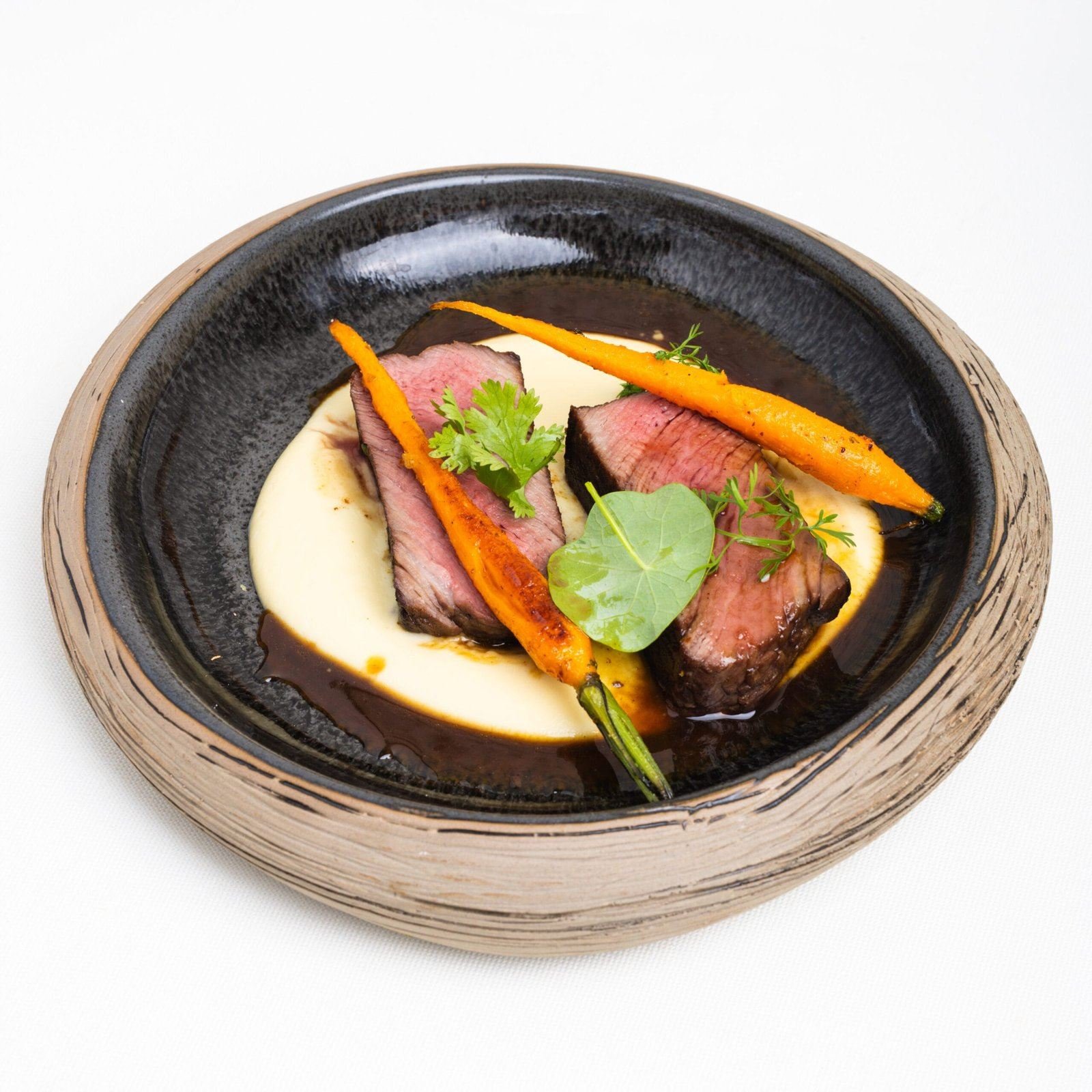 Filet de bœuf rosé, carottes rôties et purée dans un bol noir et grès