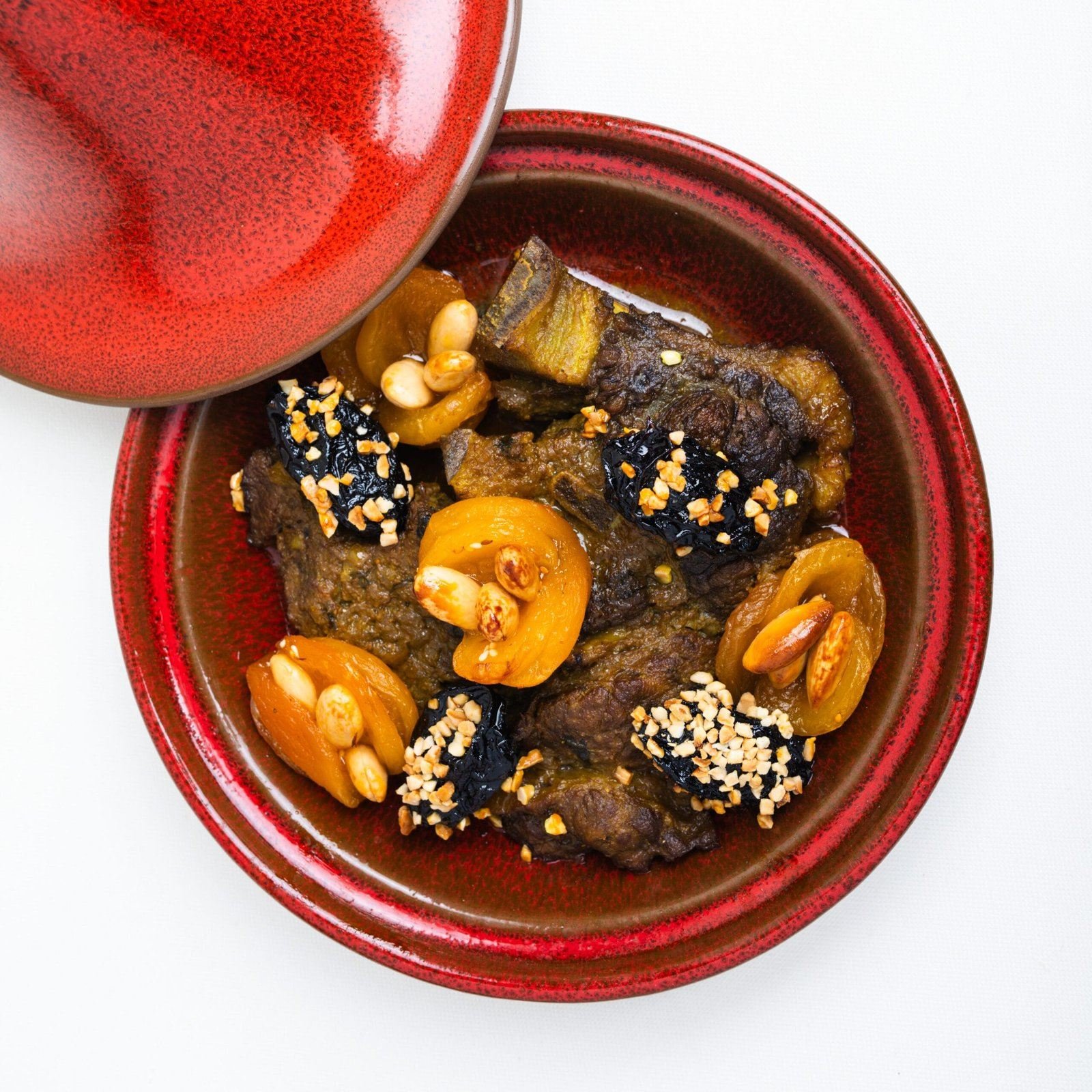 Tajine rouge ouvert, viande, pruneaux, amandes et sésame noir