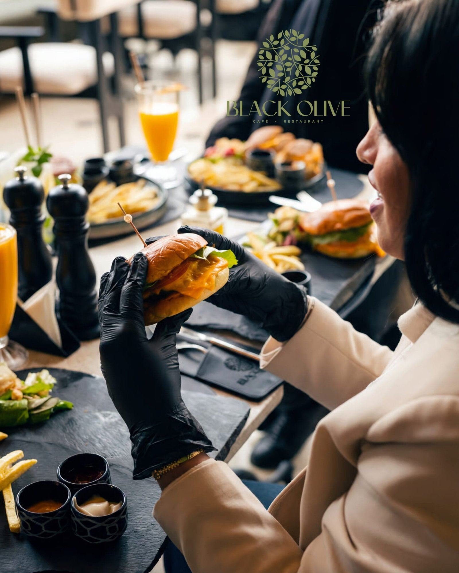 Une cliente tient un burger, frites et sauces sur la table