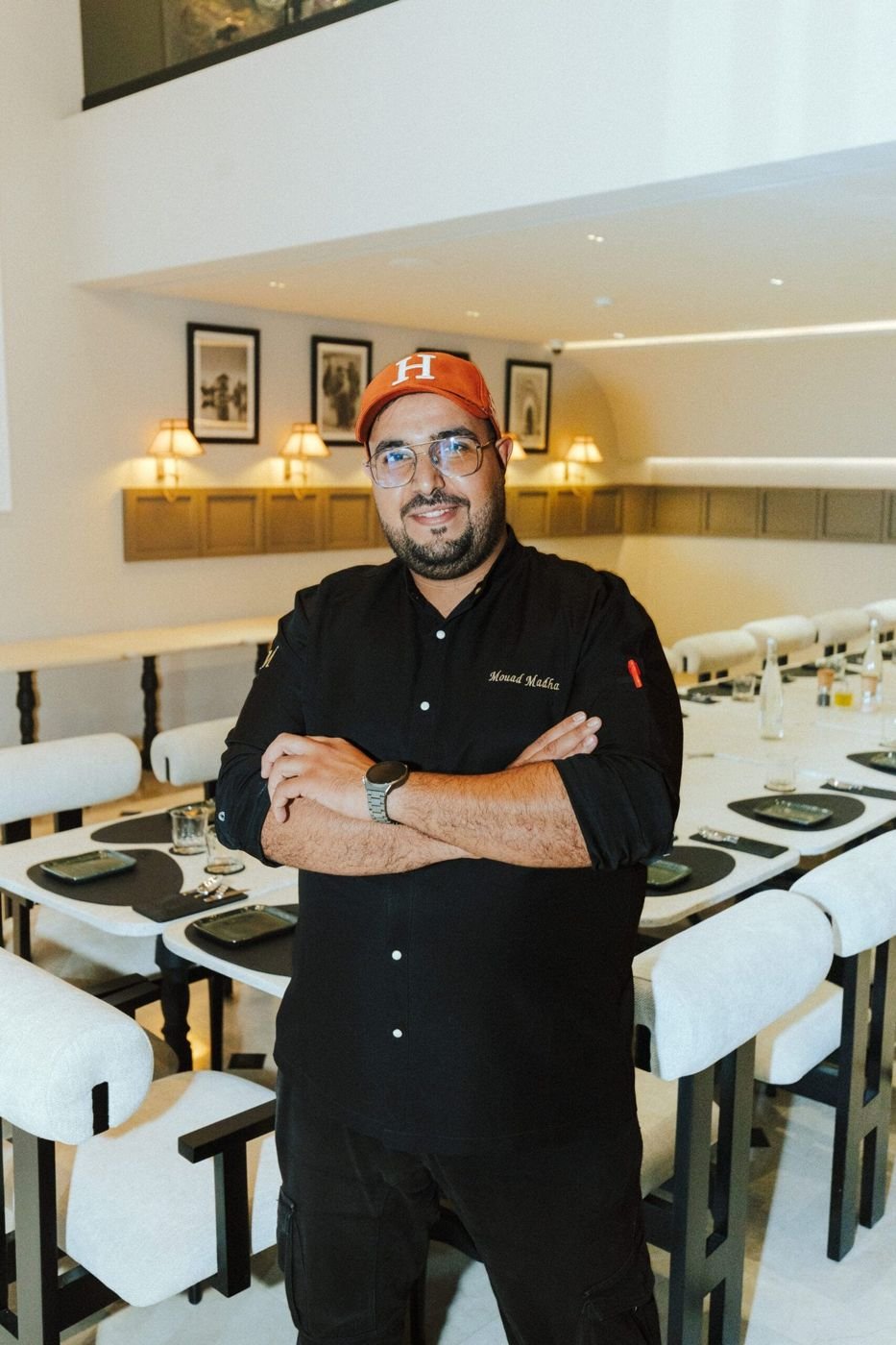 Un chef en tenue noire, bras croisés, dans la salle du restaurant