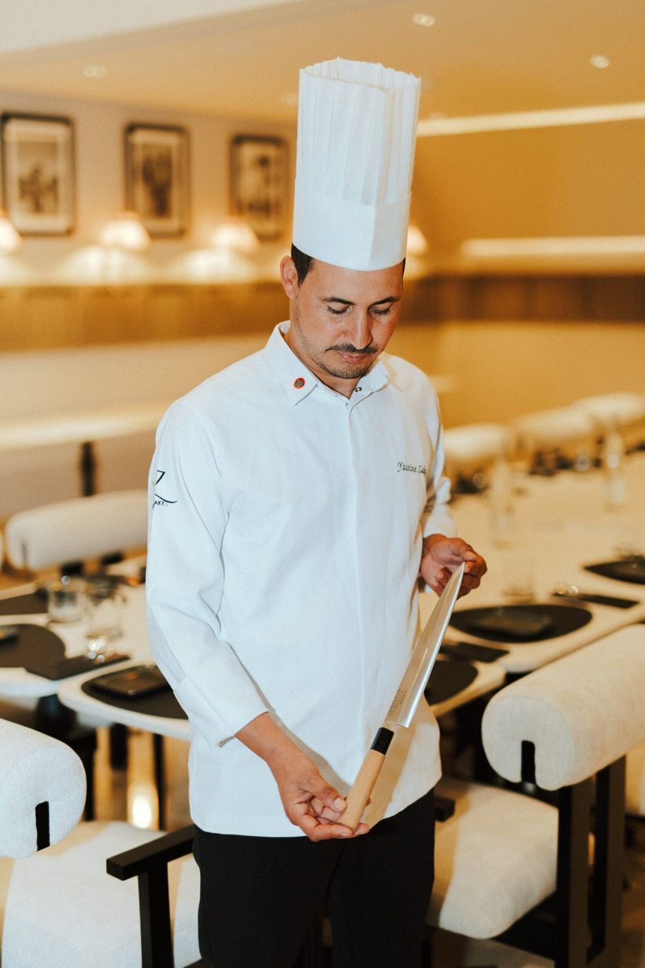 Un chef en tenue blanche tenant un couteau devant les tables dressées