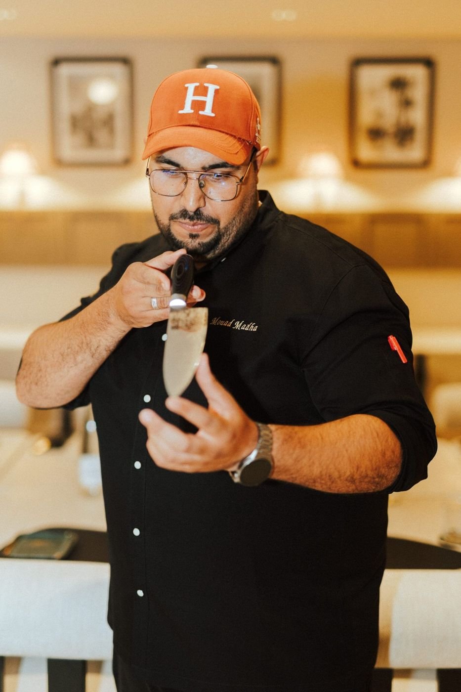 Un chef en tenue noire examinant une lame, dans la salle du restaurant